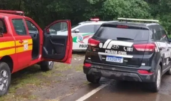 Veículos da polícia e bombeiros parados na estrada, com um deles com a porta aberta.