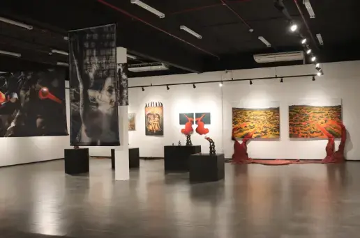 Espaço expositivo com obras de arte em paredes, esculturas e painéis em um ambiente de iluminação controlada.