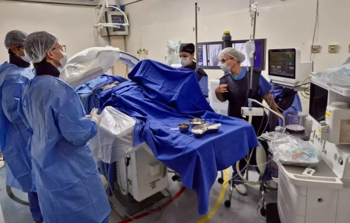 Equipe médica em sala de cirurgia, com foco em procedimentos intervencionistas, utilizando equipamentos e vestindo roupas adequadas.