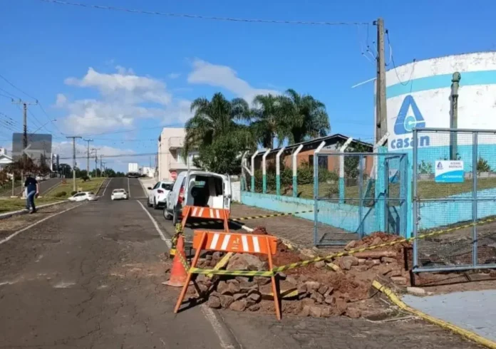 Bloqueio na rua com faixas de sinalização, barreiras de pedras e veículo estacionado ao fundo.