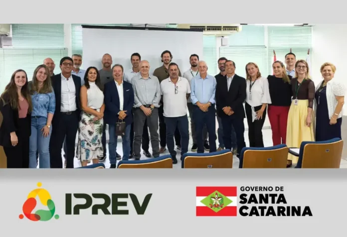 Grupo de pessoas em ambiente interno, em frente a um datashow, com logotipos do IPREV e Governo de Santa Catarina ao fundo.