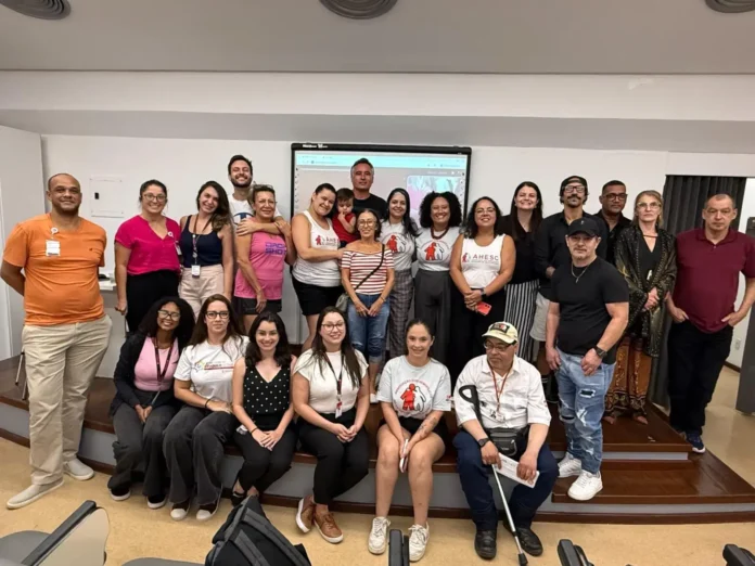 Grupo de pessoas posando em um ambiente interno, com painel ao fundo e camisetas com logo da AHESC.