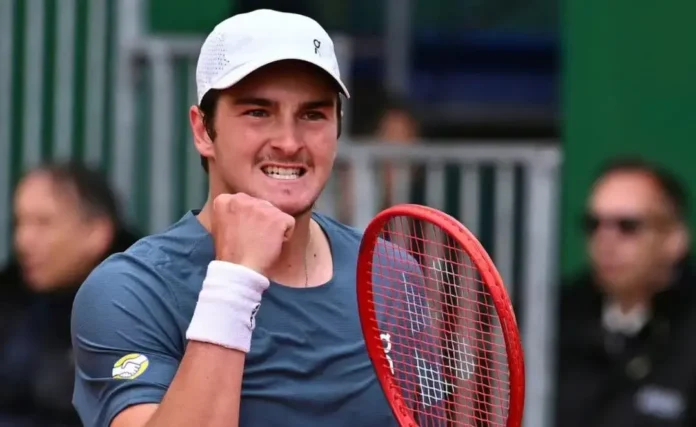 Atleta comemora com um punho cerrado, segurando uma raquete de tênis, em ambiente de competição.