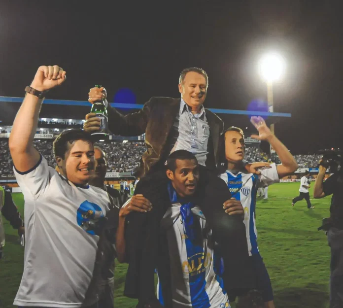 Celebration no campo com quatro pessoas comemorando, uma delas sendo carregada sobre os ombros, segurando uma garrafa.