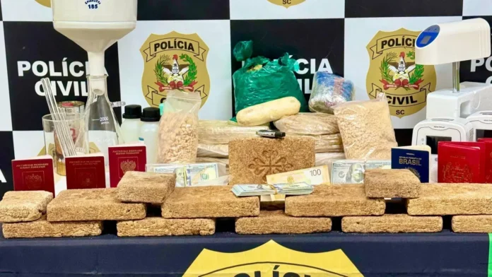 Diversos tabletes de substância suspeita, pacotes, dinheiro e passaportes em uma mesa coberta com toalha.