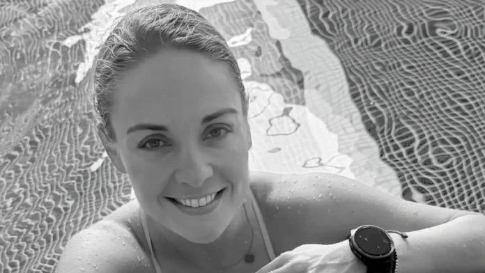 Pessoa sorrindo em uma piscina, com água visível e reflexos no fundo.