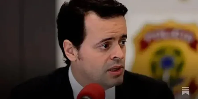 Homem com cabelo escuro e terno falando em uma conferência, com um fundo de logotipo da polícia.