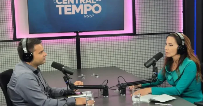 Duas pessoas sentadas em um estúdio com microfones, discutindo em frente a um banner com a inscrição "CENTRAL DO TEMPO".