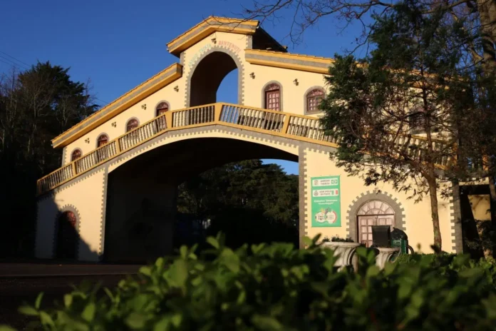 Estrutura arquitetônica em arco com janelas emolduradas e cercas, cercada por vegetação. Placa visível com informações turísticas.