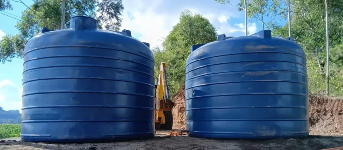 Dois reservatórios azuis grandes em uma área rural, com um equipamento de escavação ao fundo.