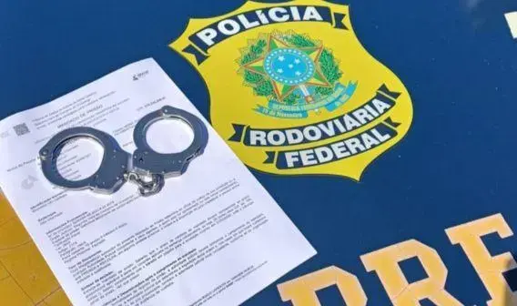 Capa de uma mesa com a logomarca da Polícia Rodoviária Federal, algemas e um documento com texto visível.