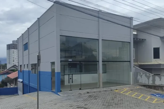 Prédio comercial moderno com fachada de vidro e paredes em azul e cinza, localizado em área urbana.
