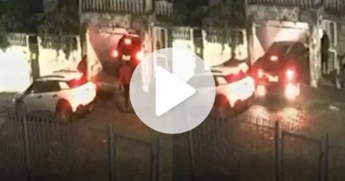 Dois carros em um embarque na garagem, um veículo preto se aproxima e um homem interage próximo.