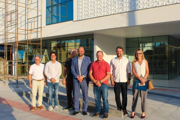Grupo de pessoas posando em frente a um edifício em construção, com estrutura metálica visível ao fundo.
