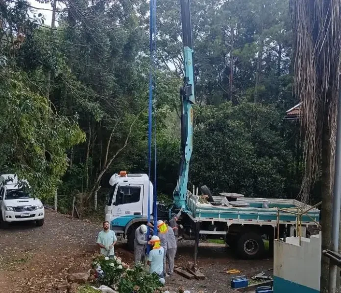Três trabalhadores em um canteiro de obras próximo a um caminhão com guindaste em um ambiente florestal.