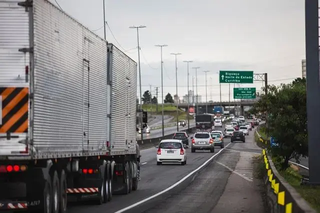 Trânsito em rodovia com caminhão e carros, sinalização indicando direção para diversos destinos, incluindo Curitiba.