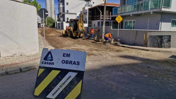 Sinalização de obras com a palavra "EM OBRAS" e trabalhadores em atividade, utilizando máquinas e ferramentas em uma rua.