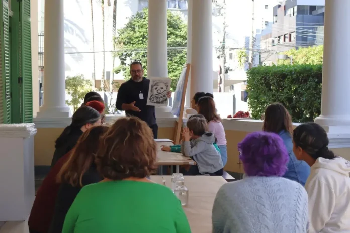 Homem instruindo um grupo de pessoas em oficina de desenho, mostrando uma ilustração em papel.