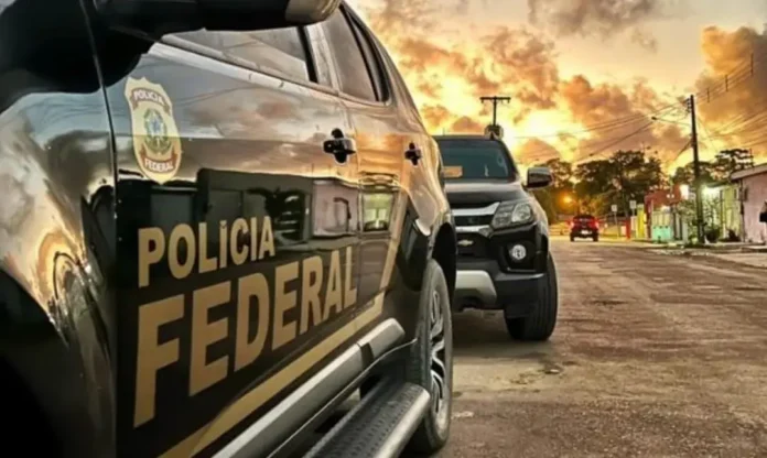 Veículo da Polícia Federal estacionado em uma rua, com outro carro ao fundo e céu avermelhado ao entardecer.