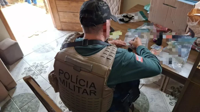 Agente da polícia militar registrando informações em uma mesa com documentos e dinheiro visíveis.