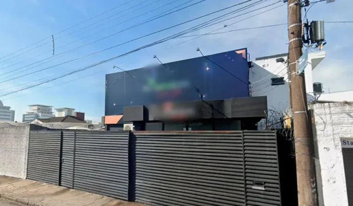 Fachada de um estabelecimento com uma grande parede publicitária, cercada por uma estrutura de segurança.