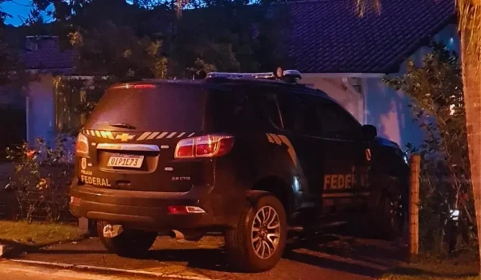 Veículo da Polícia Federal estacionado em frente a uma residência durante a noite.