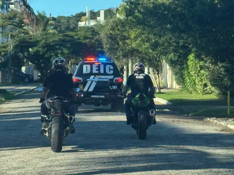 Grupo de amigos parados ao lado de um carro em estrada, com paisagem verde ao fundo e céu claro.
