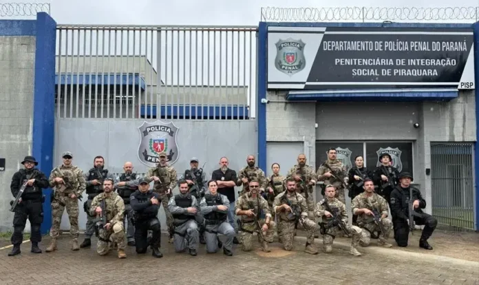 Trinta membros da equipe da Polícia Penal, armados, posam em frente à Penitenciária de Piraquara.