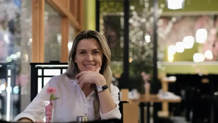Pessoa sorrindo em um restaurante com decoração interna elegante e flores ao fundo.