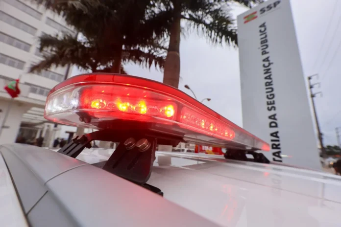 Luz de sirene de viatura em primeiro plano com o edifício da Secretaria da Segurança Pública ao fundo.