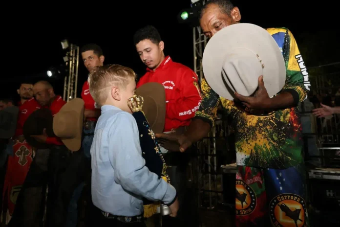 Criança recebe um troféu de mãos de um adulto, enquanto outros participantes aguardam ao fundo.