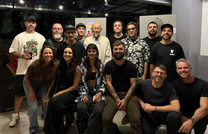 Grupo de pessoas posando para foto em ambiente interno, com paredes claras e obras de arte ao fundo.