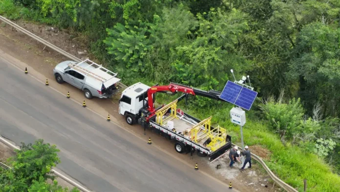Veículo e caminhão ao lado da estrada com equipamentos e painéis solares para instalação.