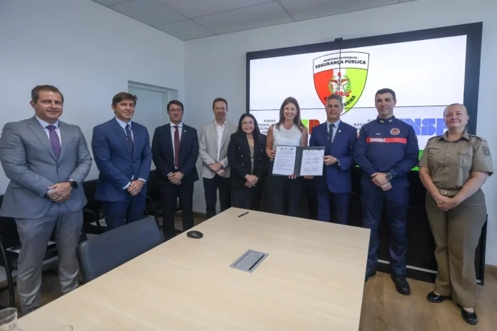 Grupo de pessoas em uma sala, posando em frente a um telão, segurando documentos relacionados à segurança pública.
