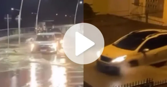 Veículos trafegando em ruas alagadas durante a noite, com água acumulada nas pistas.