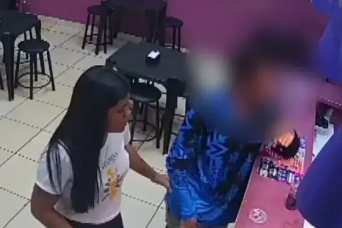 Duas pessoas em um ambiente interno, uma mulher interagindo com um homem próximo ao balcão.