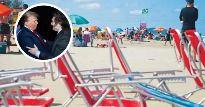 Praia lotada com várias pessoas deitadas e em pé, guarda-sóis coloridos e cadeiras vazias na areia.