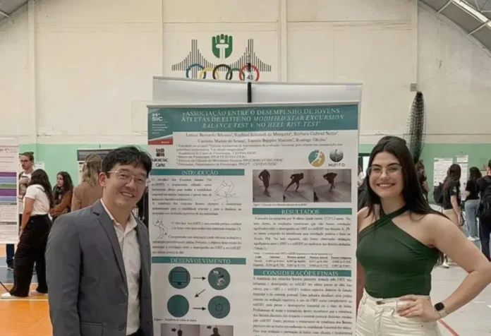 Pessoas sorrindo ao lado de um pôster de pesquisa em evento acadêmico, com gráficos e texto visíveis.