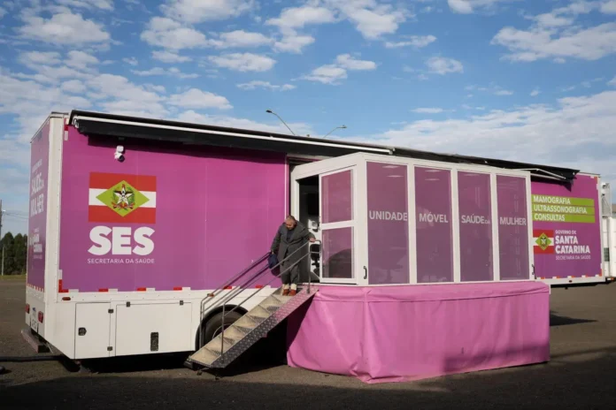 Unidade móvel da saúde com ênfase em mamografia e ultrassonografia, sinalizada em tons de rosa e informações da Secretaria da Saúde.