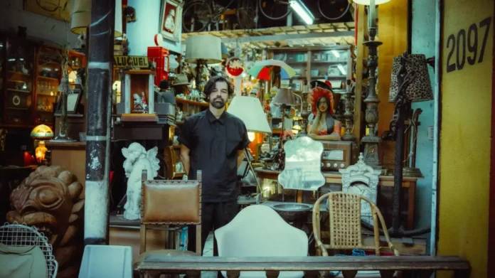 Pessoas em um espaço de antiquários cercado por móveis, objetos decorativos e esculturas.