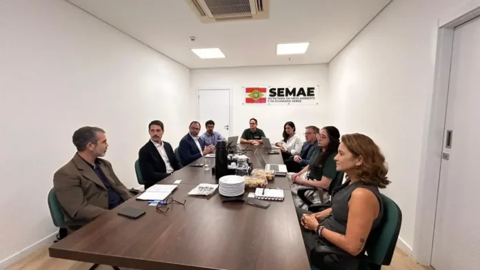 Reunião em mesa longa com várias pessoas sentadas, exibindo logo da SEMAe na parede.