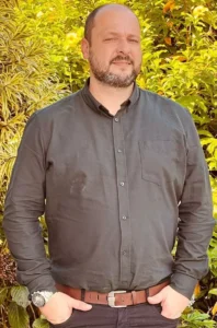 homem branco calvo vestindo camisa e calça sociais de cor cinza escuro